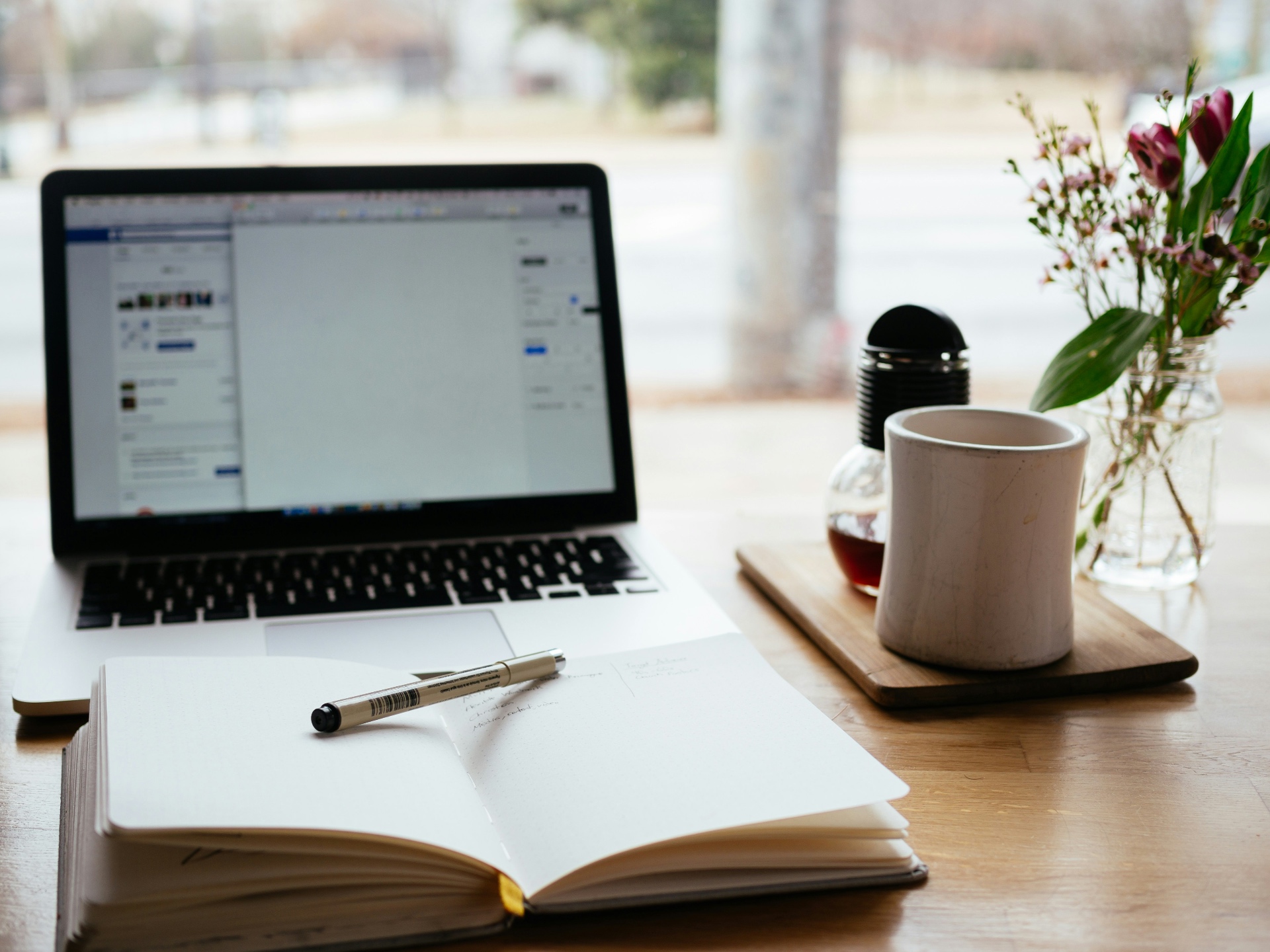 Organized workspace with open laptop, notebooks, pen and coffee cup on a light wooden table, conveying a professional work atmosphere