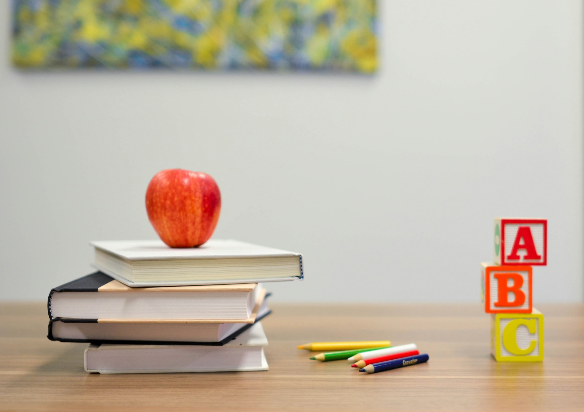 Schreibtisch mit aufgeschlagenen Büchern, bunten Stiften, Holzklötzen mit ABC-Buchstaben und Lernmaterialien, die eine einladende Bildungsumgebung darstellen