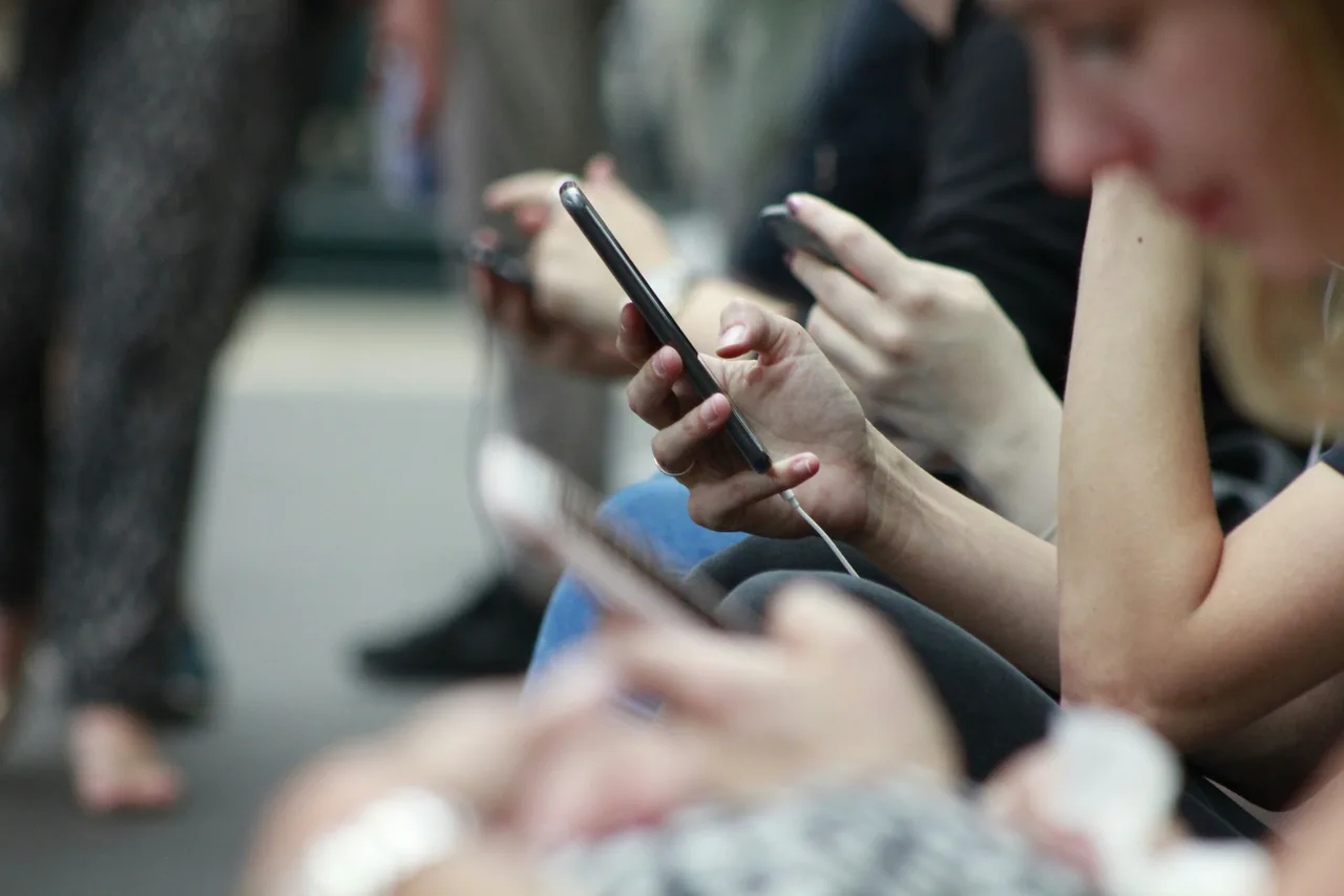 Several people sitting side by side looking at their smartphones